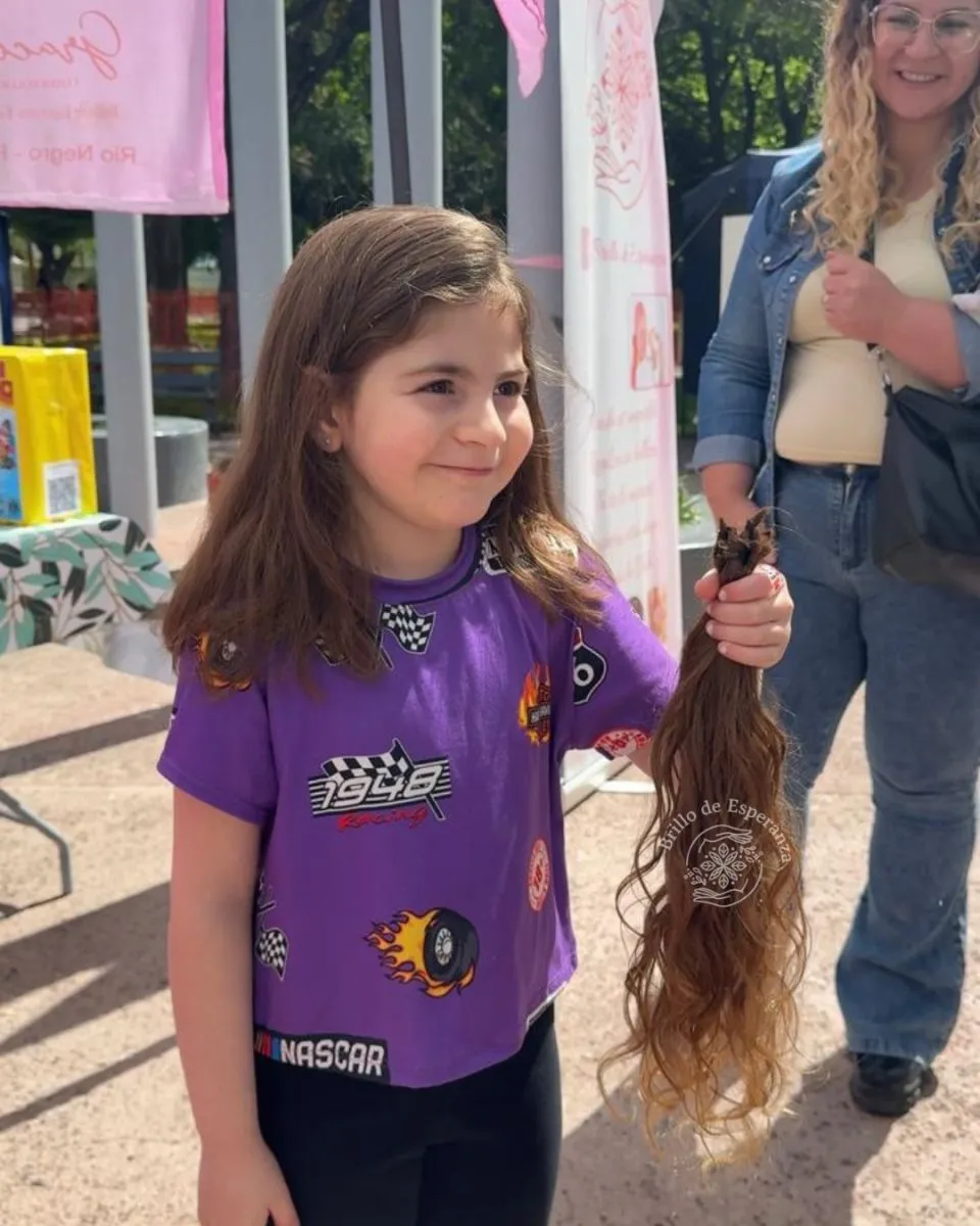 Regina posando junto al cabello que donó, detrás su madre orgullosa. Foto: Brillo de Esperanza